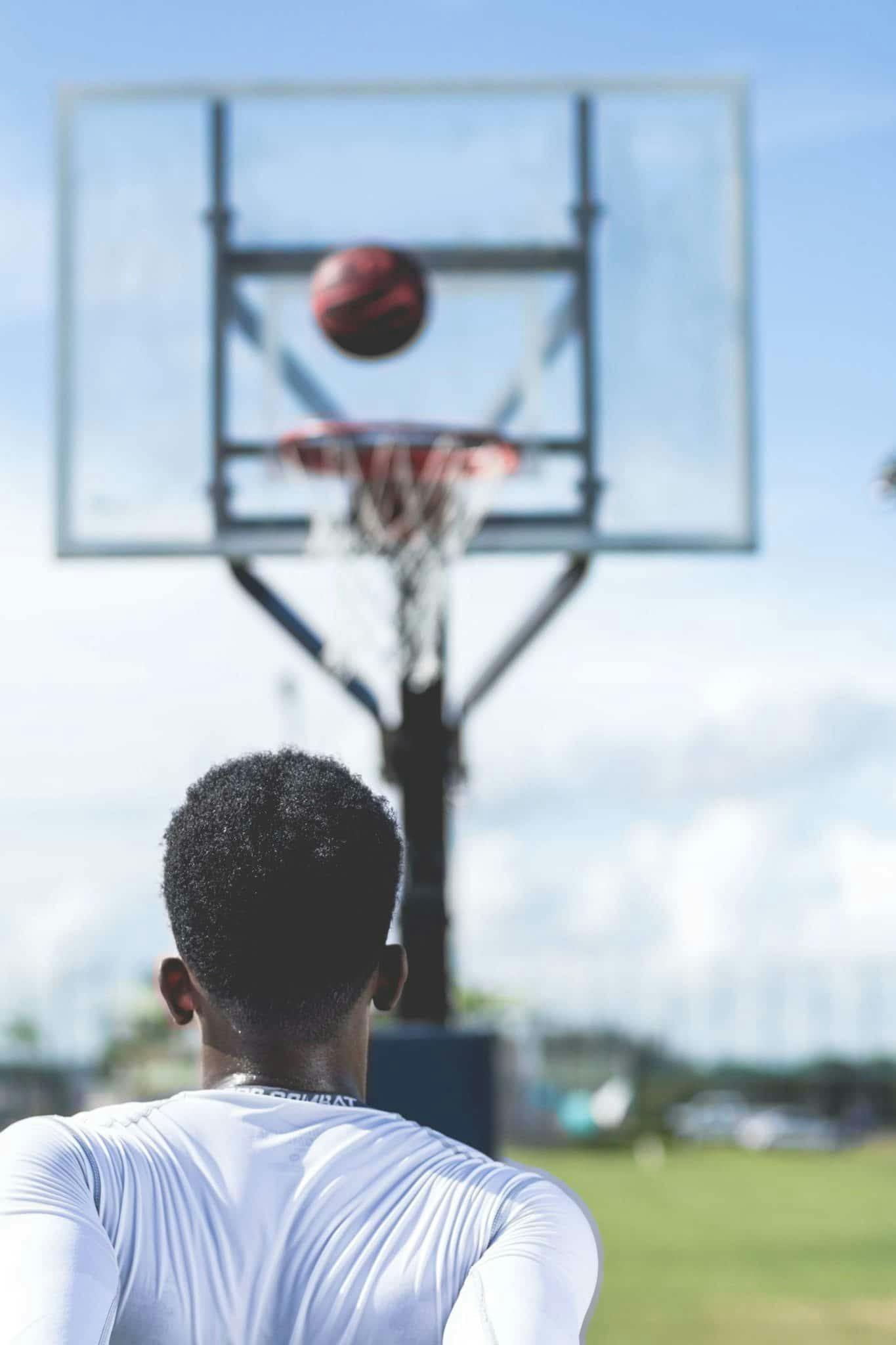 A young athlete focuses on shooting a basketball, enjoying an outdoor game on a sunny day.